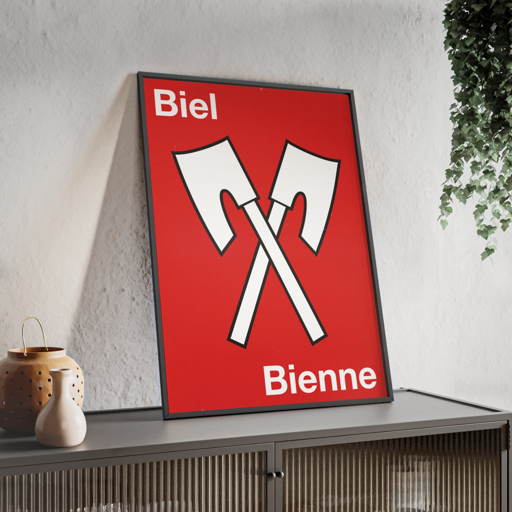 Minimalist framed wall poster of the Biel Bienne coat of arms featuring crossed white axes on a red background, displayed in a natural pinewood frame.