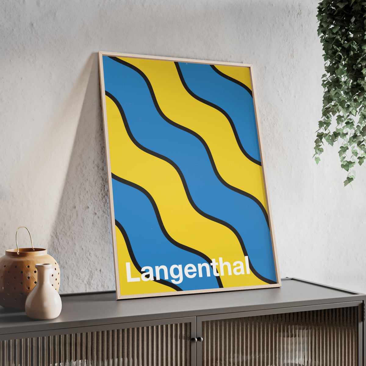 Minimalist framed poster of the Langenthal coat of arms featuring blue and yellow wavy stripes, set in a natural wood frame on an interior console table.