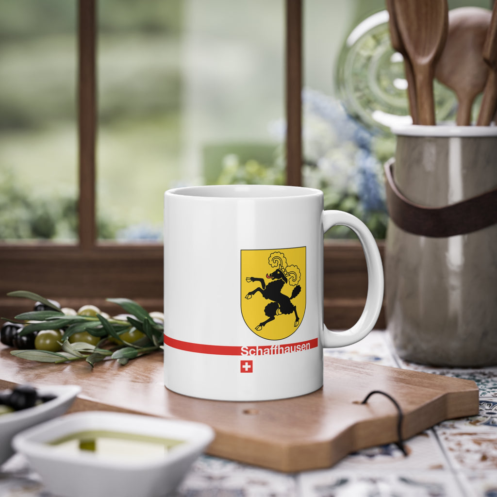 White ceramic mug featuring the golden Canton of Schaffhausen coat of arms with a black ram, a modern red horizontal line with 'Schaffhausen' text, and a small Swiss cross below.