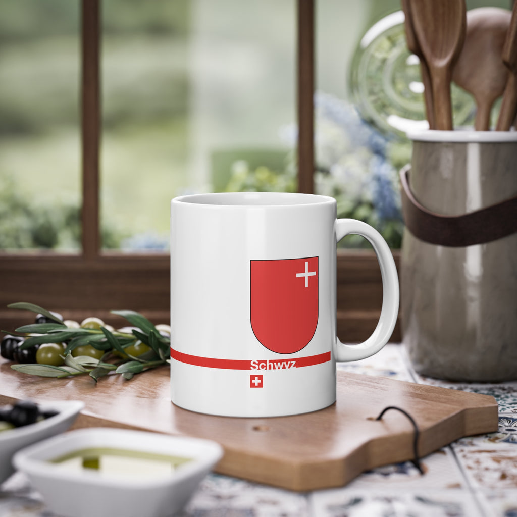 White ceramic mug featuring the red Canton of Schwyz coat of arms with a small white cross, a modern red horizontal line with 'Schwyz' text, and a small Swiss cross below.