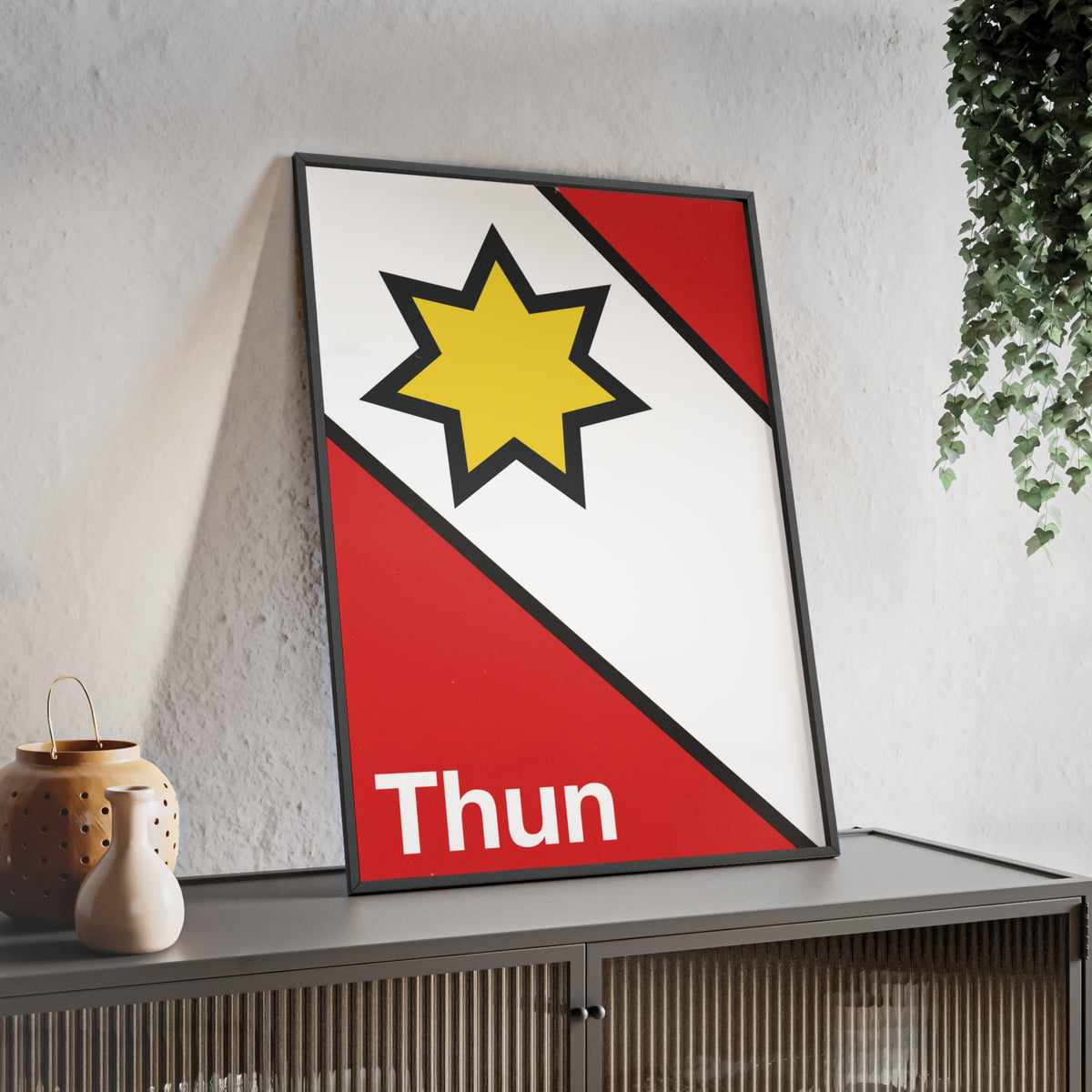 Minimalist framed poster of the Thun coat of arms featuring a yellow star on red and white diagonal fields, displayed in a natural wood frame on a console table.