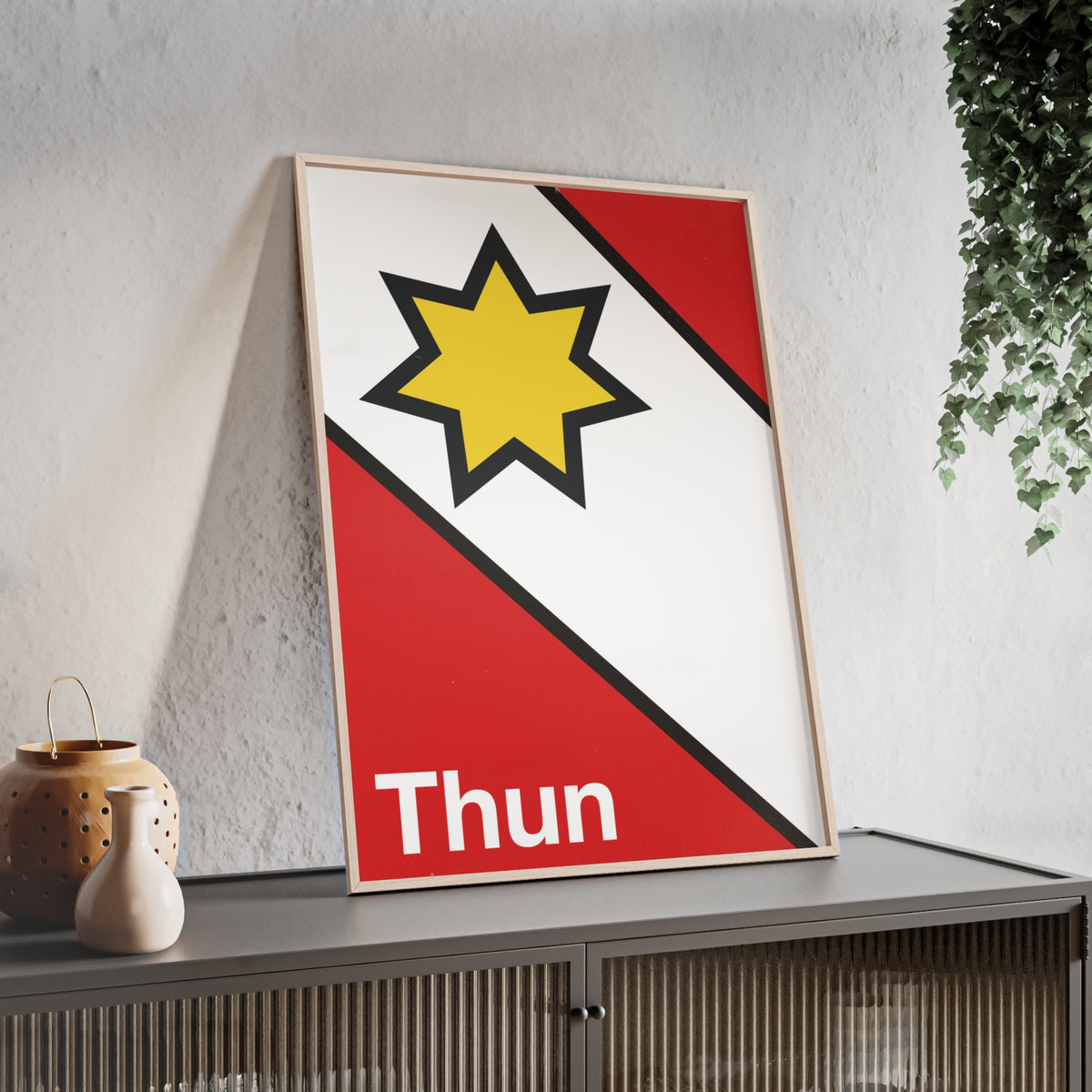 Minimalist framed poster of the Thun coat of arms featuring a yellow star on red and white diagonal fields, displayed in a natural wood frame on a console table.