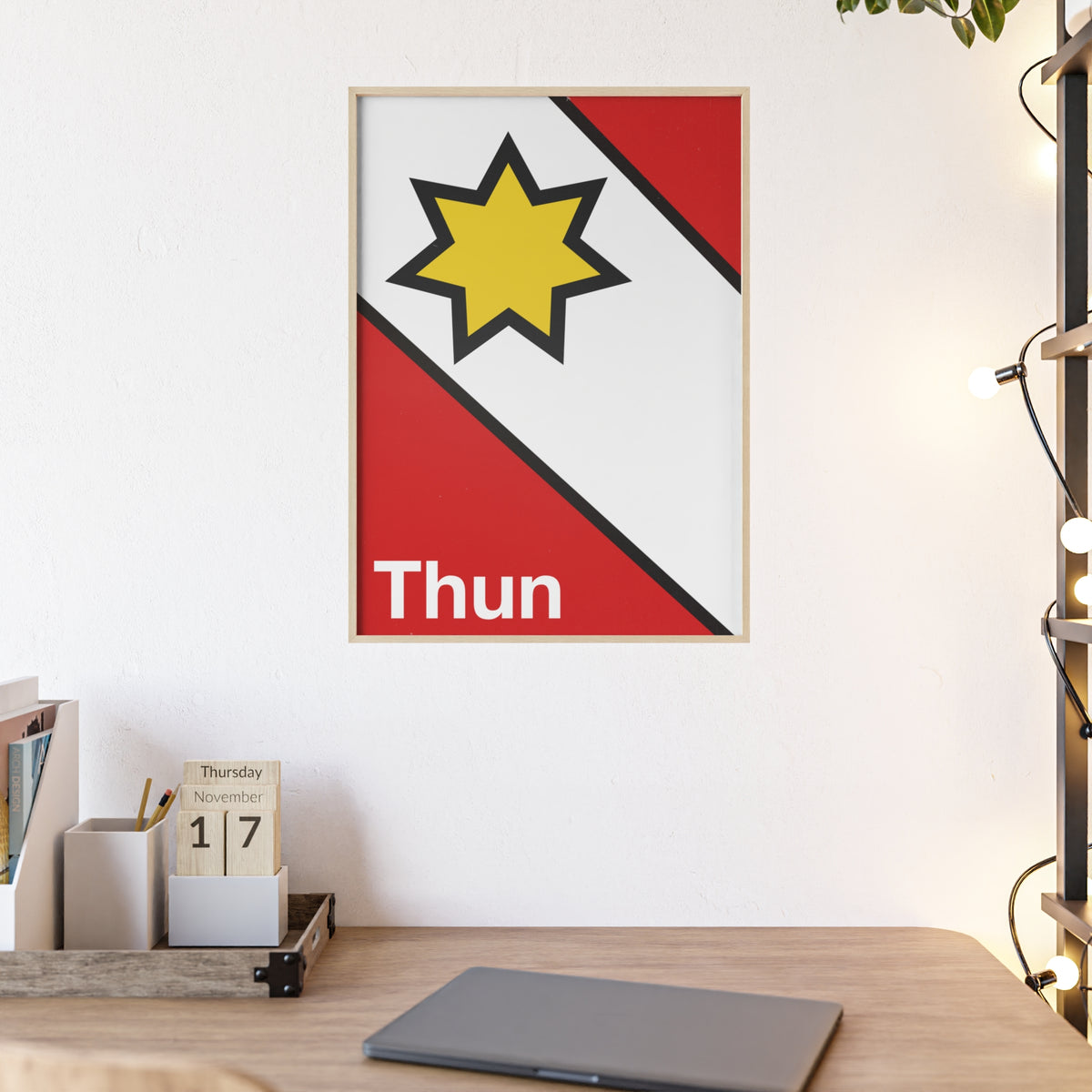 Minimalist framed poster of the Thun coat of arms featuring a yellow star on red and white diagonal fields, displayed in a natural wood frame on a console table.
