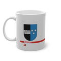 White ceramic mug with the vertically divided coat of arms of the Canton of Aargau (black with silver waves and blue with stars), featuring a modern red line and a small Swiss cross.
