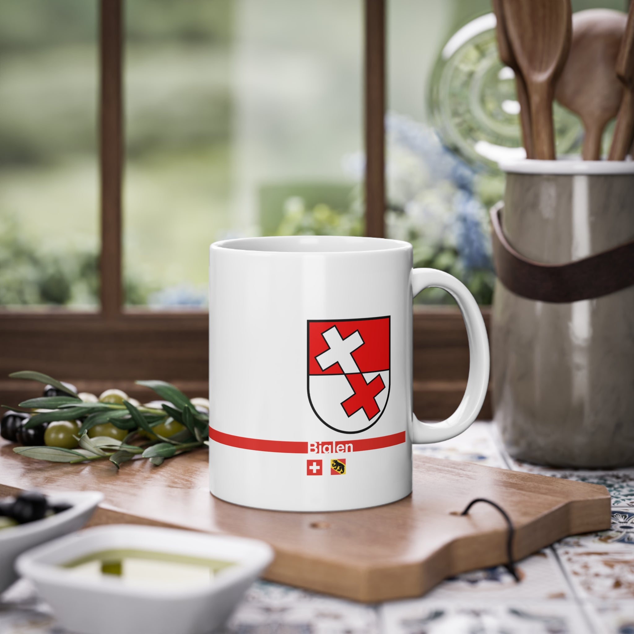 White ceramic mug featuring the red and white split coat of arms of the Biglen Commune, a modern red horizontal line with 'Biglen' text, and small Swiss and Bernese bear flags below.