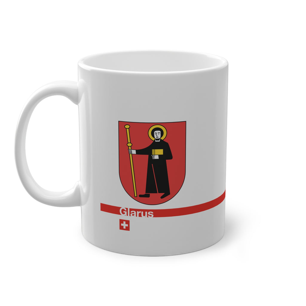 White ceramic mug with the red Canton of Glarus coat of arms featuring Saint Fridolin, a modern red line with 'Glarus' text and a small Swiss cross.
