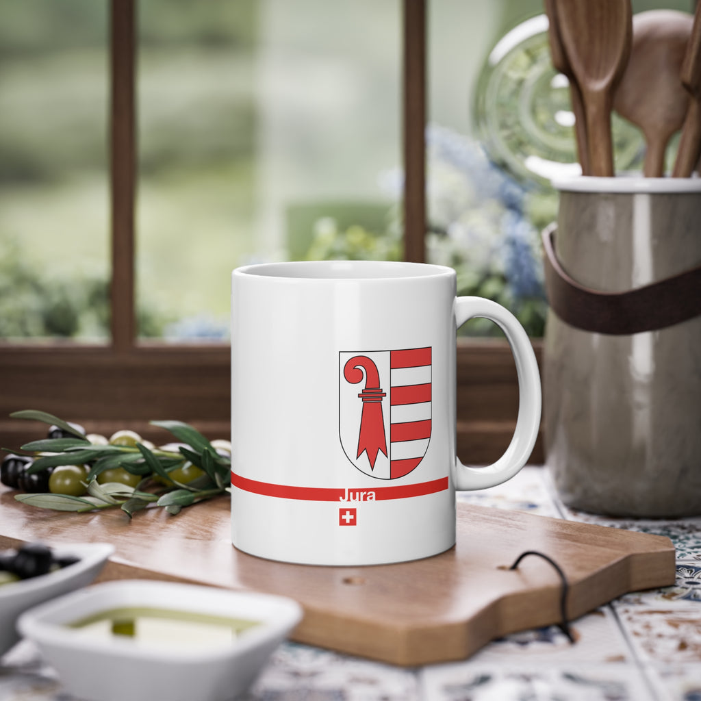 White ceramic mug featuring the red and white Canton of Jura coat of arms (bishop's crosier and seven stripes), a modern red horizontal line with 'Jura' text, and a small Swiss cross below.