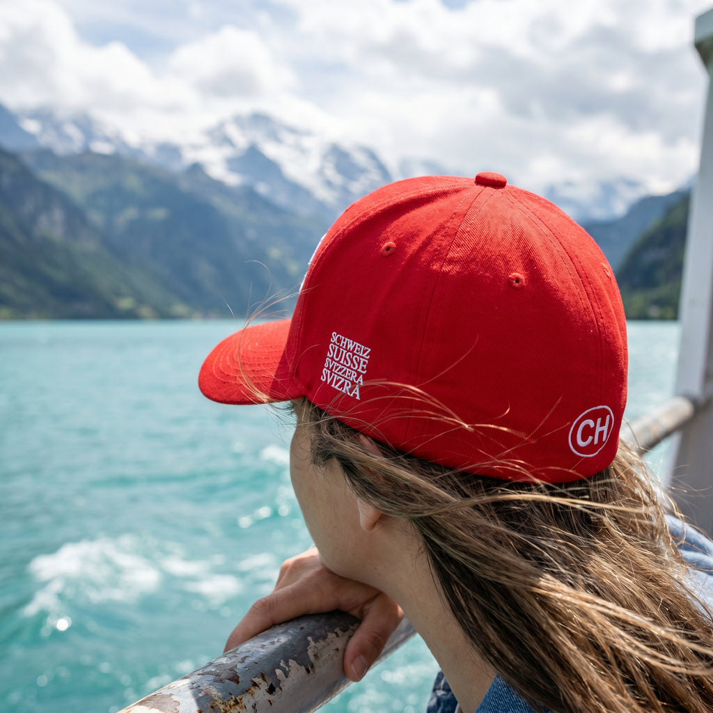 Product multi-angle mockup views of a premium red structured Swiss baseball cap. Front features white 'SWITZERLAND GREAT SINCE 1291' embroidery. Right side displays the Swiss cross flag, left side features country names in German, French, Italian, and Romansh, and the closed back shows a circular CH logo.