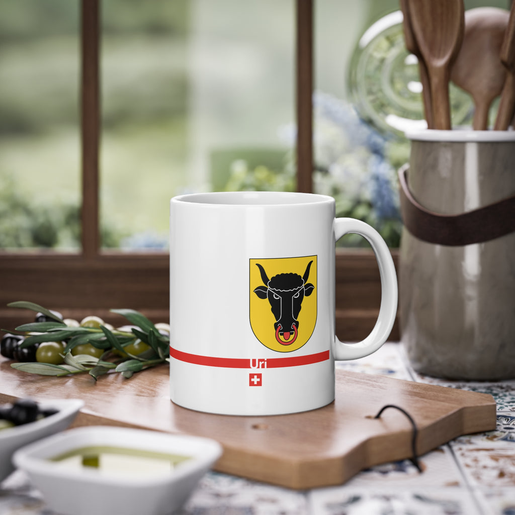 White ceramic mug featuring the golden Canton of Uri coat of arms with a black bull's head and red nose ring, a modern red horizontal line with 'Uri' text, and a small Swiss cross below.