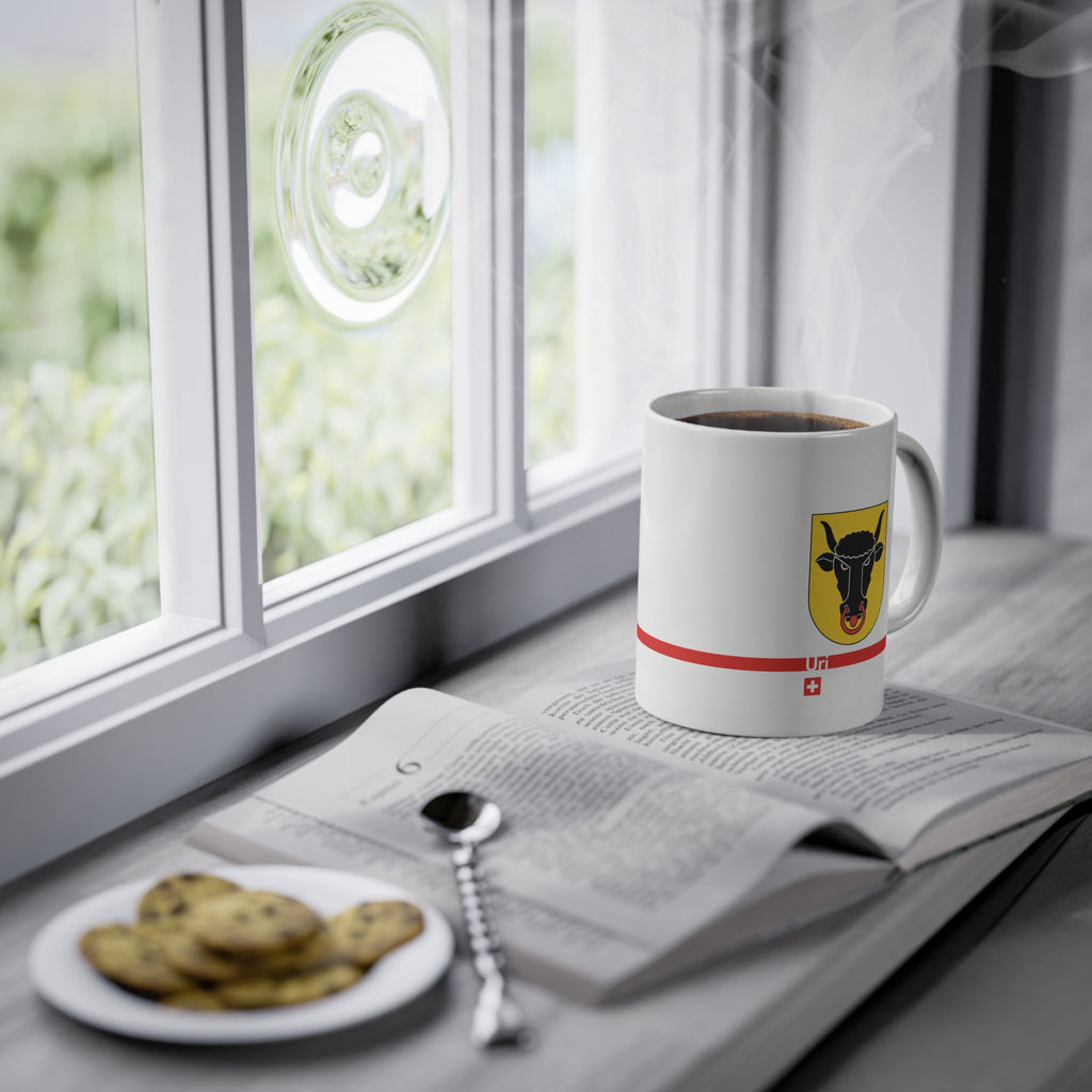 White ceramic mug featuring the golden Canton of Uri coat of arms with a black bull's head and red nose ring, a modern red horizontal line with 'Uri' text, and a small Swiss cross below.