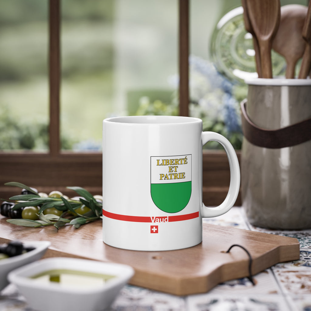 White ceramic mug featuring the white and green Canton of Vaud coat of arms with golden 'Liberté et Patrie' text, a modern red horizontal line with 'Vaud' text, and a small Swiss cross below.