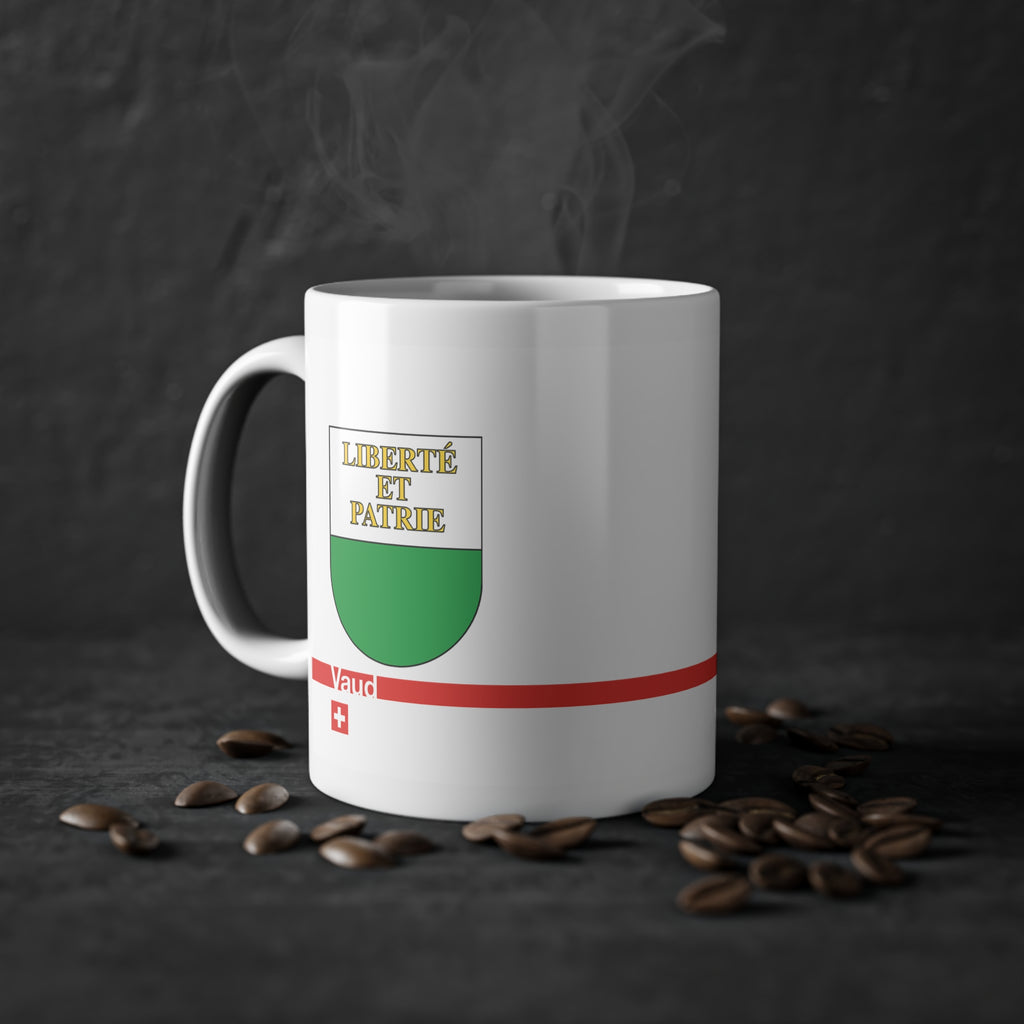 White ceramic mug featuring the white and green Canton of Vaud coat of arms with golden 'Liberté et Patrie' text, a modern red horizontal line with 'Vaud' text, and a small Swiss cross below.